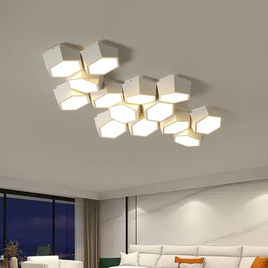 A modern white geometric cluster ceiling light with hexagonal panels emitting a soft white light, mounted on a white ceiling in a contemporary living room with a sofa visible.