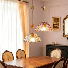 A set of colored glass butterfly pendant lights suspended over a dining table with upholstered chairs.