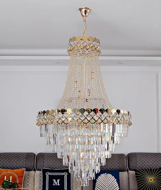 A grand, multi-tiered gold chandelier with cascading crystal elements, illuminated against a neutral ceiling.