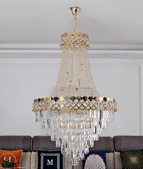 A grand, multi-tiered gold chandelier with cascading crystal elements, illuminated against a neutral ceiling.