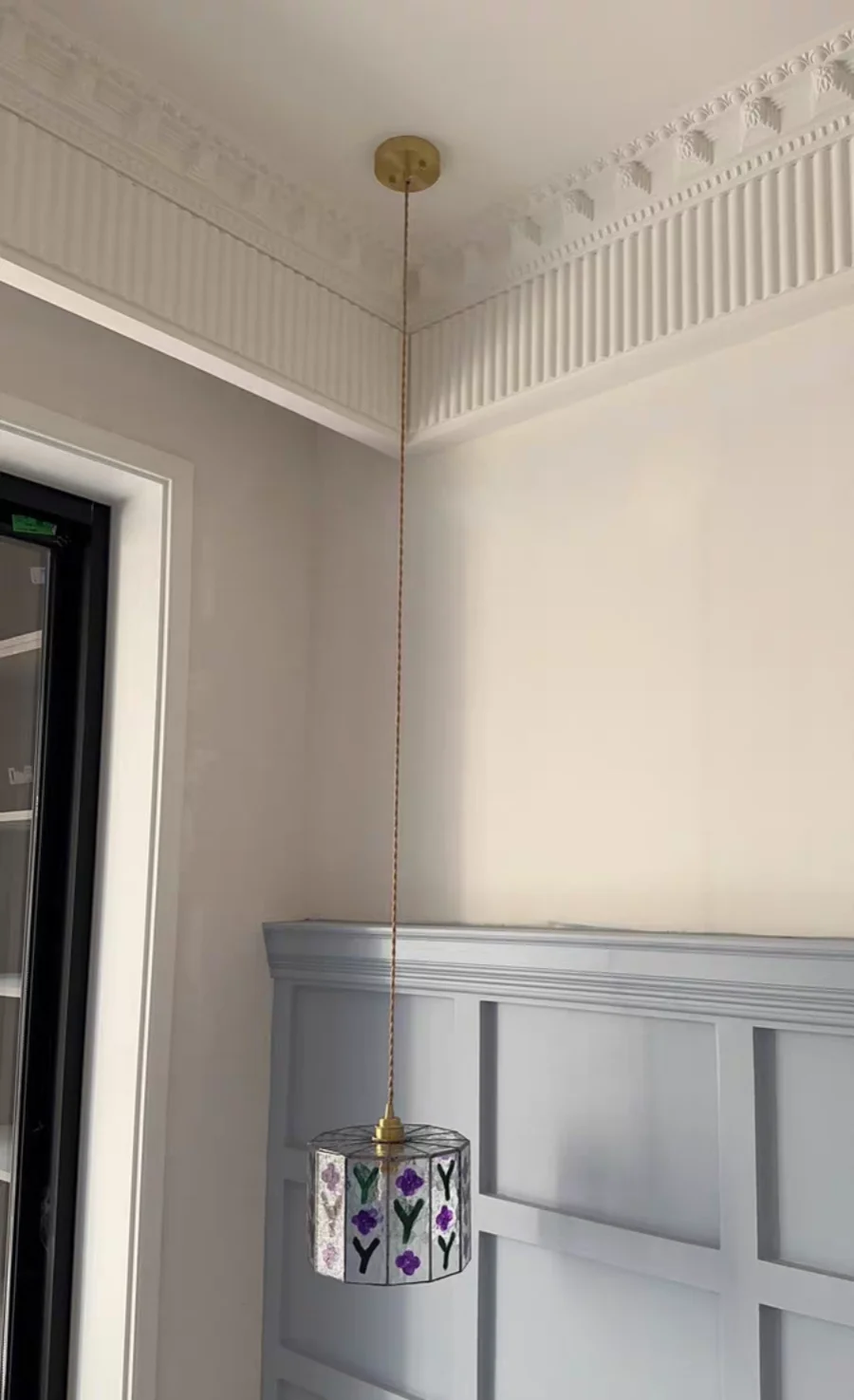 Pendant light fixture with decorative shade in a room with white walls and molding.