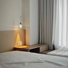 Glass globe pendant light with moon detail installed above a bed, casting a warm glow on the wooden headboard and bedside table.