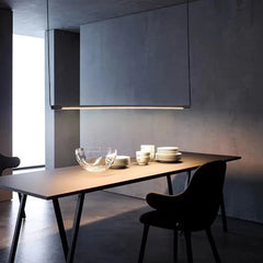 Black minimalist linear pendant light casting light on a modern dining table setting