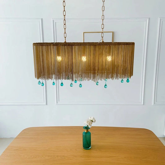 Gold chain pendant light with blue teardrop crystals hanging above a wooden table