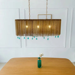 Gold chain pendant light with blue teardrop crystals hanging above a wooden table