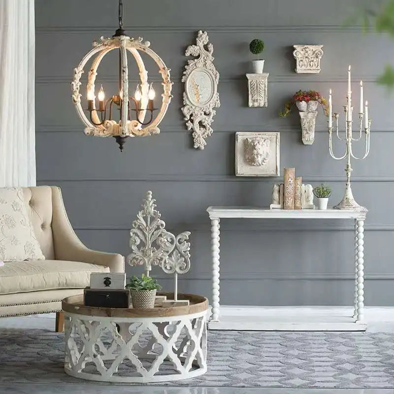 A living room scene featuring a distressed white carved wood globe chandelier hanging above a coffee table with decorative items.