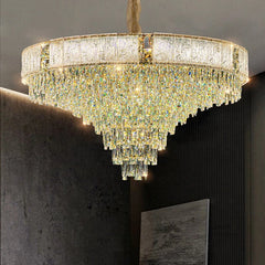 A luxurious gold chandelier with multiple tiers of cascading clear crystals against a dark background.
