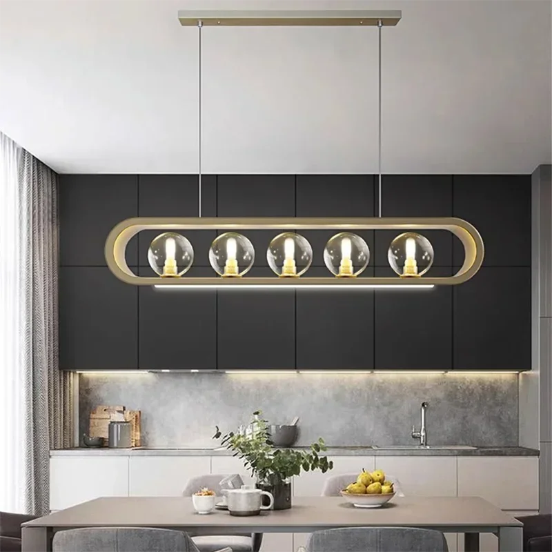 Modern gold linear pendant light with clear glass globes and an integrated LED light bar, mounted in a kitchen setting.