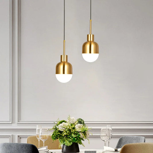 Two gold metal dome pendant lights hanging above a dining table, each with a white light emitting from the bottom.