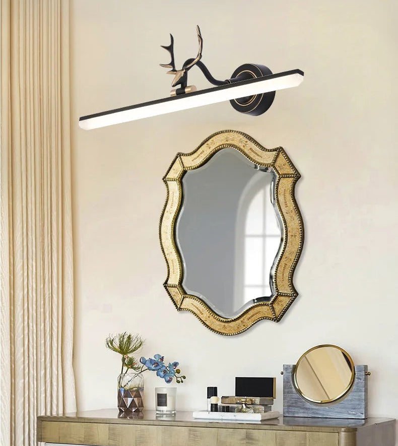 Decorative wall mirror with gold frame and modern light fixture on a beige wall.