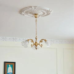 A gold chandelier with three frosted glass flower-shaped shades, suspended from a white ceiling with decorative molding.