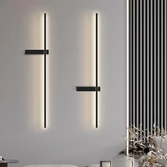 Two black minimalist LED strip wall sconces with warm lighting shown on a grey wall next to a decorative panel.