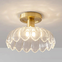 Close-up of a gold flush mount ceiling light with a clear glass shade shaped like flower petals, emitting a warm glow.