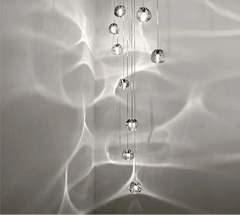 A long cascade of clear crystal ball pendant lights hanging against a textured wall, creating light reflections.