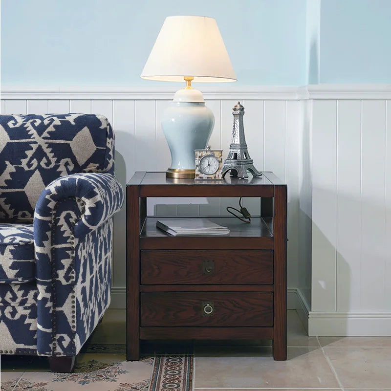 A light blue ceramic table lamp with a cream drum shade sits on a dark wood side table next to a sofa.