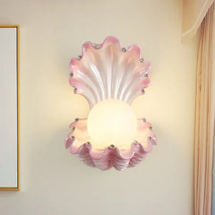 Pink seashell wall sconce with a frosted globe light and small crystal accents, mounted on a cream-colored wall.