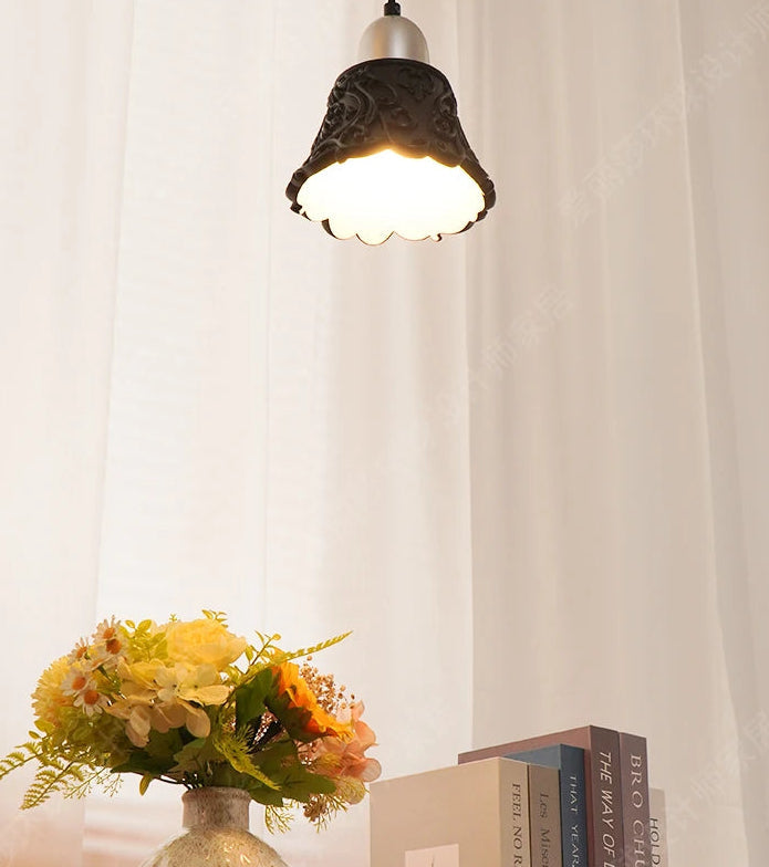 Decorative pendant light above a vase with flowers and books on a wooden surface.