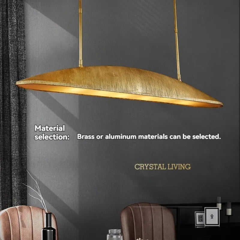 A brass linear pendant light with a textured surface suspended from the ceiling