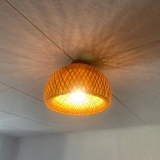 Dome-shaped bamboo ceiling light fixture casting a patterned shadow on a white tiled ceiling.