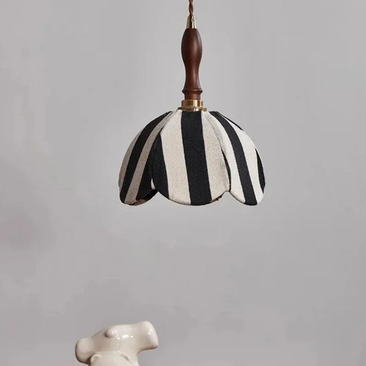 A black and white striped fabric pendant light hangs against a neutral background, showcasing its scalloped edge and wooden top.