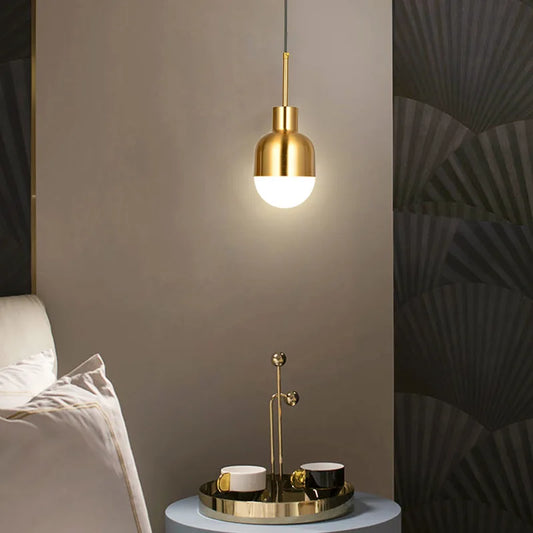 A single gold metal dome pendant light illuminating a bedside table with a small tray and cups.