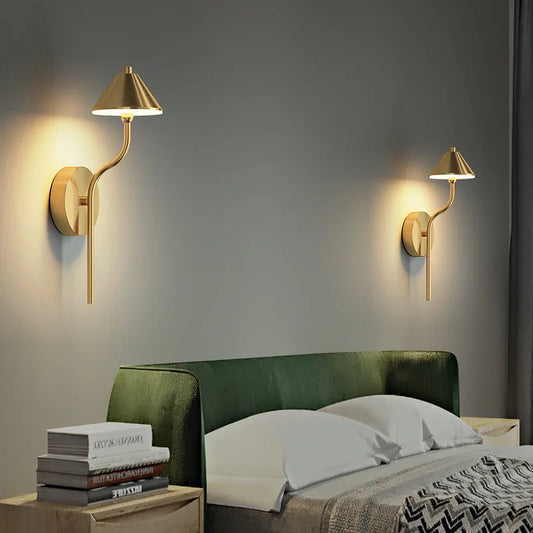 Brass modern mushroom wall sconce mounted on a gray wall above a green headboard.