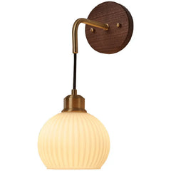 Close-up of a wall sconce with a round walnut wood base, a curved brass arm, and a ribbed frosted glass globe shade.