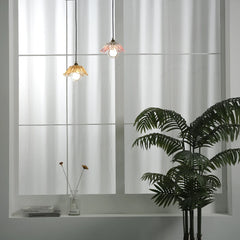 Two colorful glass pendant lights hanging in front of a large window with sheer curtains.