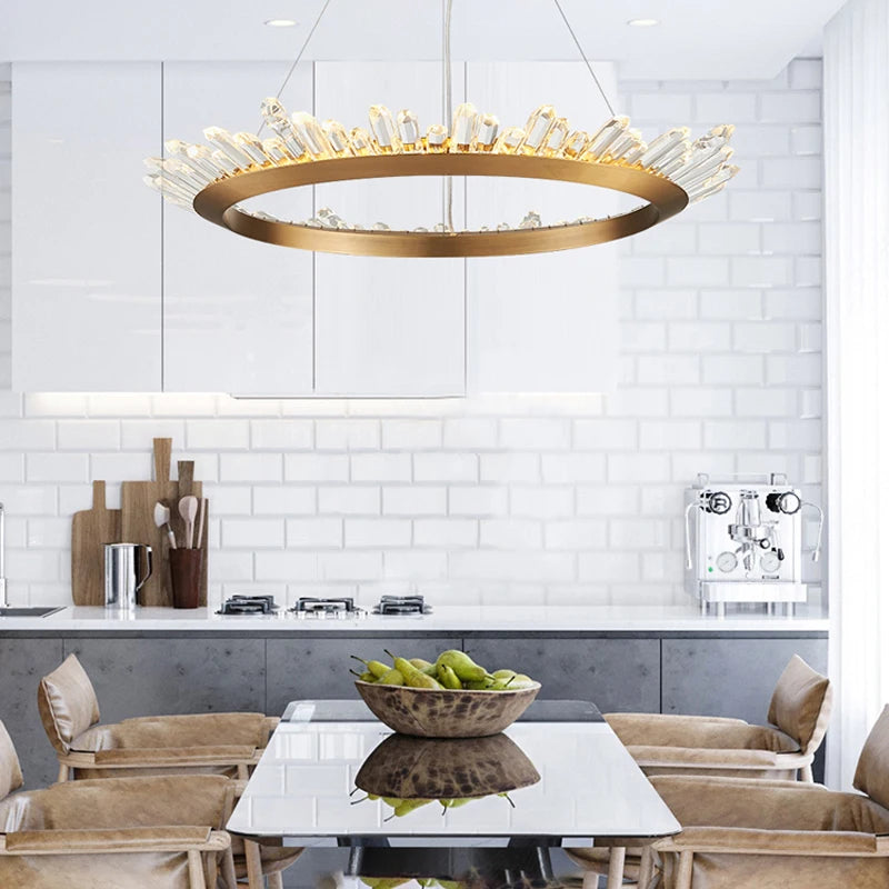 Modern kitchen with a gold pendant light fixture, white tiled walls, and a dining table with fruit.