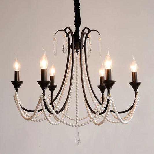 Close-up view of a black, multi-arm chandelier showcasing its intricate pearl bead strands and crystal accents, with a few of the candelabra bulbs illuminated.