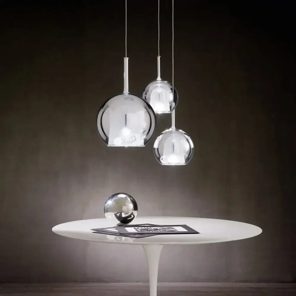 Three chrome-finished globe pendant lights hanging over a white table with a decorative sphere.