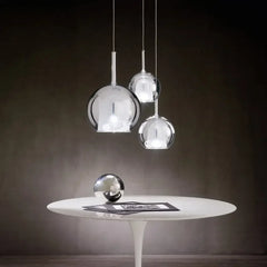 Three chrome-finished globe pendant lights hanging over a white table with a decorative sphere.