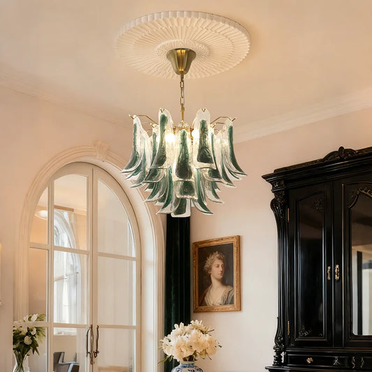 A gold-tone tiered chandelier with green and clear glass accents hanging from a decorative ceiling medallion in an elegantly decorated room.