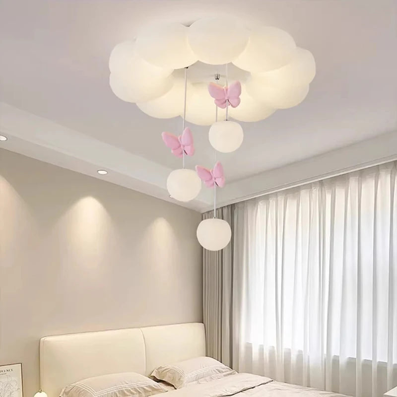 A white cloud-shaped ceiling light with pink butterflies and hanging orbs, illuminated in a room with curtains.