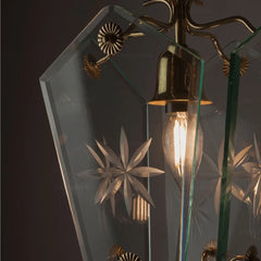 Side view of a clear glass pendant light with etched starburst patterns and brass accents, hanging against a dark background.