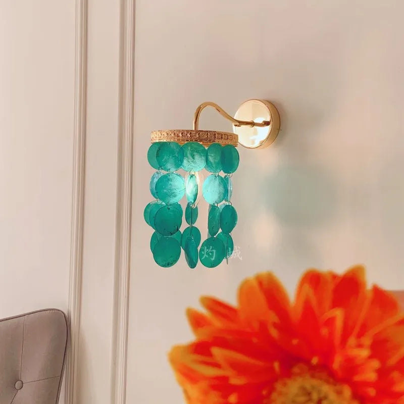 Close-up of a gold wall sconce with blue-green shell accents, showing the light diffusing through the shells.