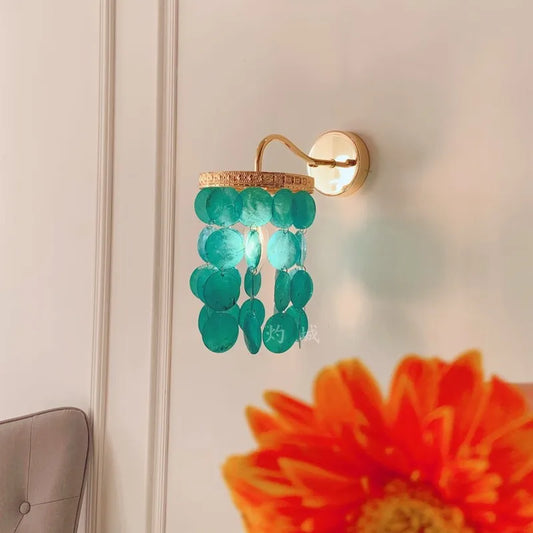 Close-up of a gold wall sconce with blue-green shell accents, showing the light diffusing through the shells.