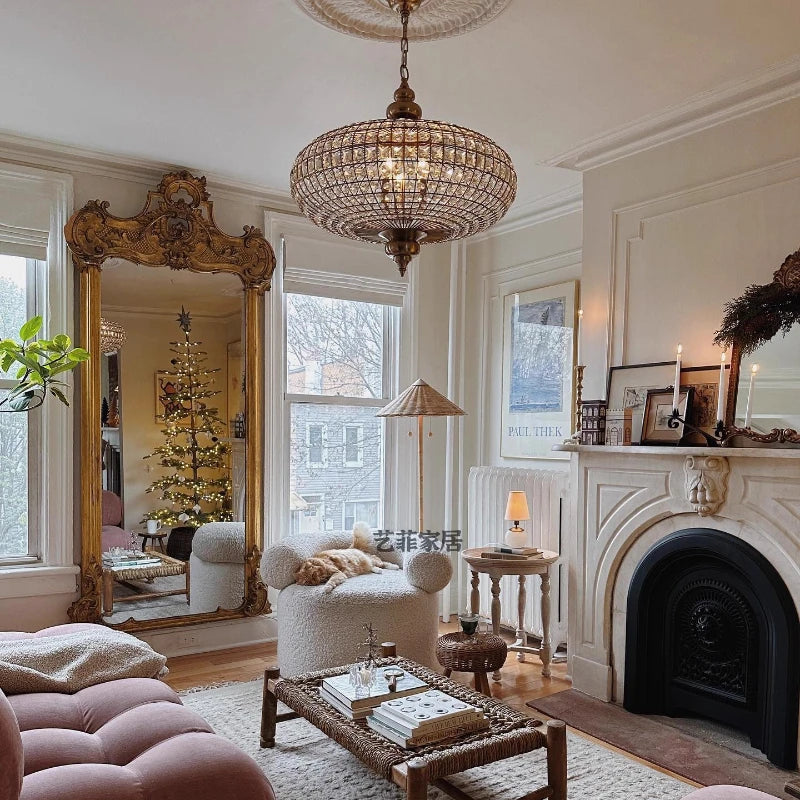 A large, ornate gold mirror reflects a Christmas tree and a living room setting, with a crystal orb chandelier hanging overhead.