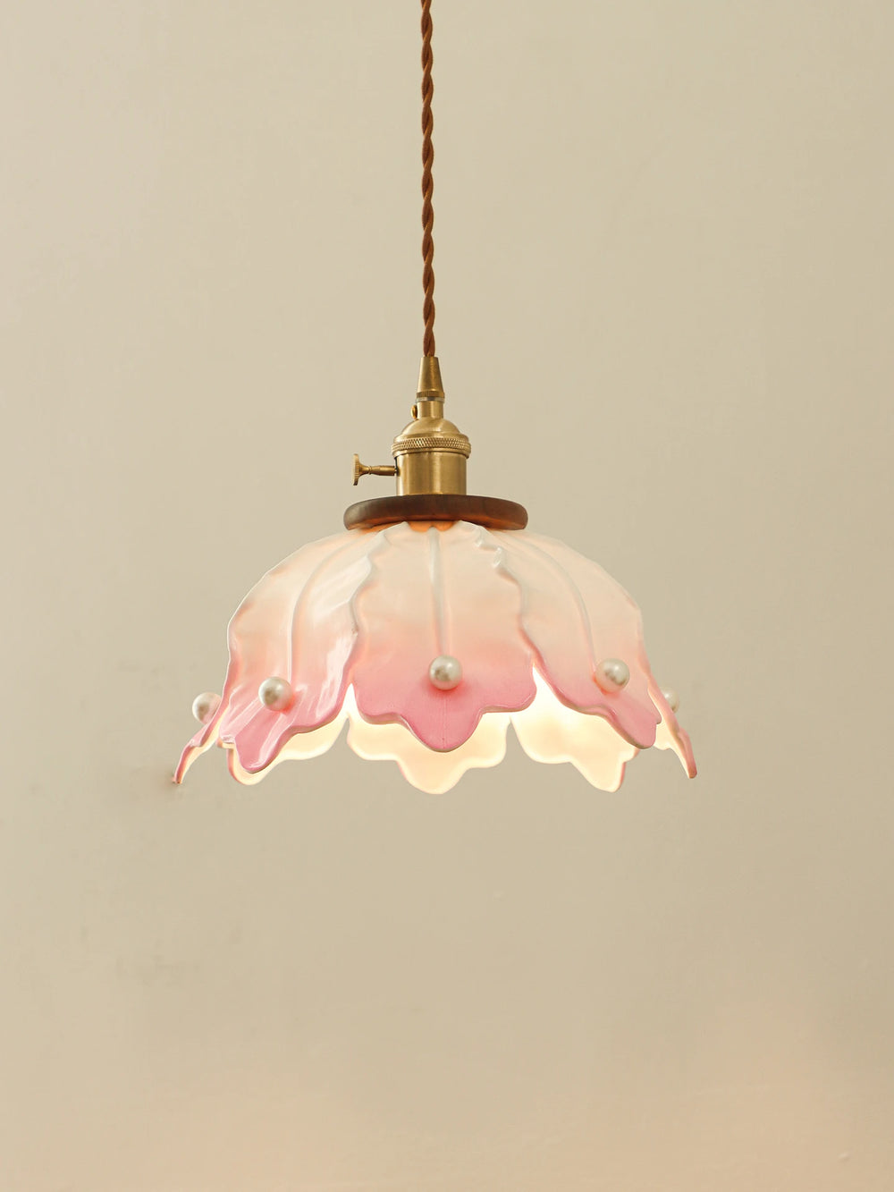 A pink and white ceramic pendant light with a petal design and pearl accents, hanging against a plain wall.