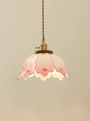 A pink and white ceramic pendant light with a petal design and pearl accents, hanging against a plain wall.