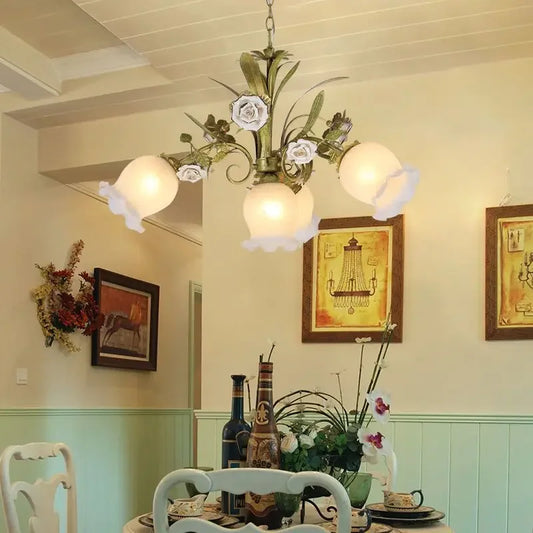 Gold floral-themed chandelier with white porcelain rose accents and frosted glass shades, hanging in a dining room setting.