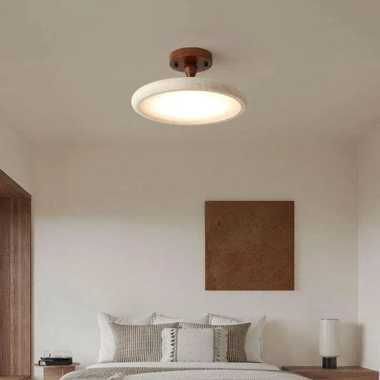 Close-up view of a round ceiling light fixture with a stone-like textured rim and a dark wood base, showing the illuminated light.