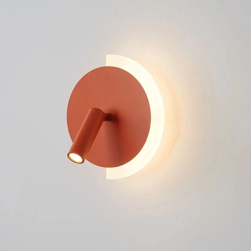 Orange modern LED wall lamp with a circular backplate and adjustable spotlight, emitting warm light against a white wall.