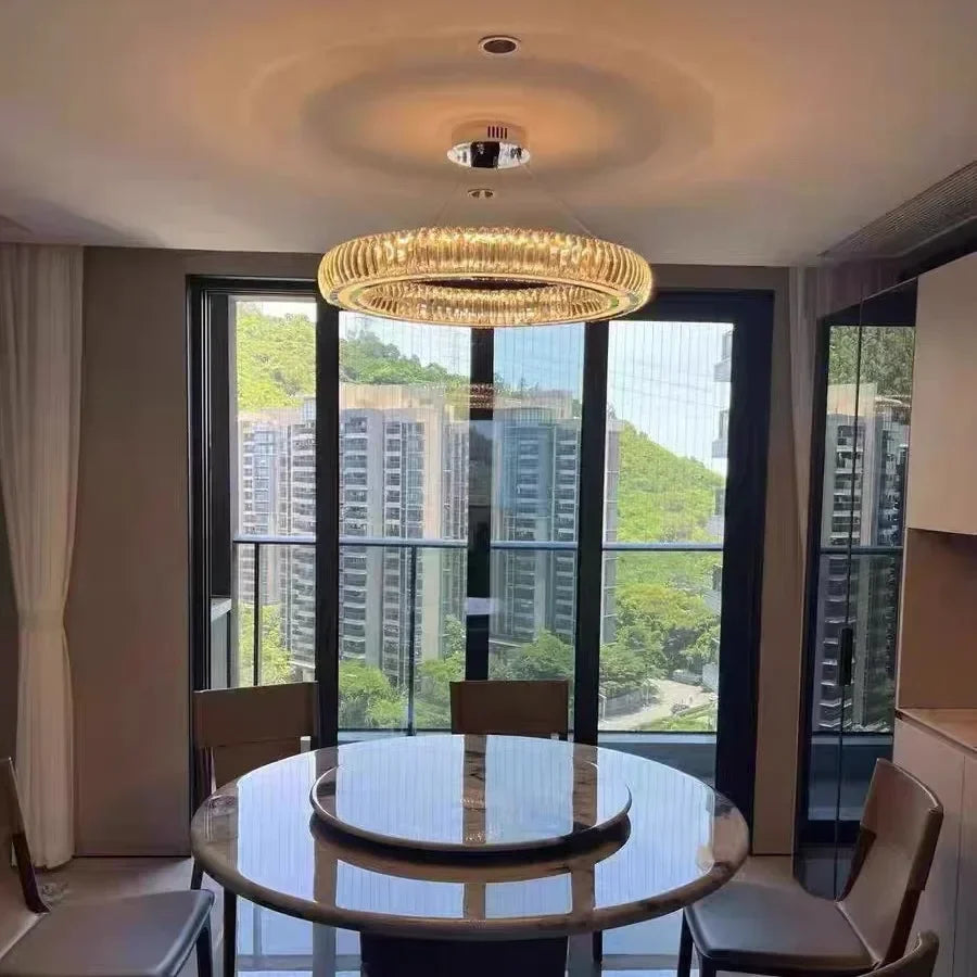 Dining room with round table and chairs, large windows showing cityscape and greenery.