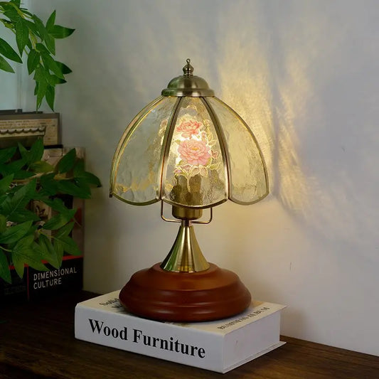 Brass table lamp with a bell-shaped glass shade featuring pink and white floral patterns, set on a wooden base.