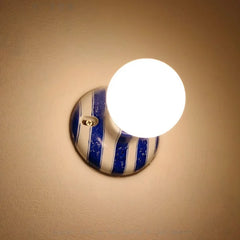 Ceramic wall sconce with blue and white stripes and a glowing round bulb.