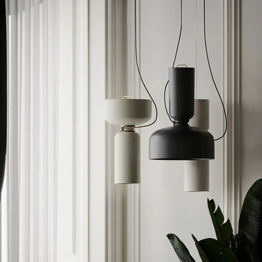 Two pendant lights, one black and one white, hanging in a room with sheer curtains in the background.