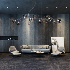 Chrome spiral wave pendant light with multiple glass globes illuminating a modern living room with a sofa and chairs.
