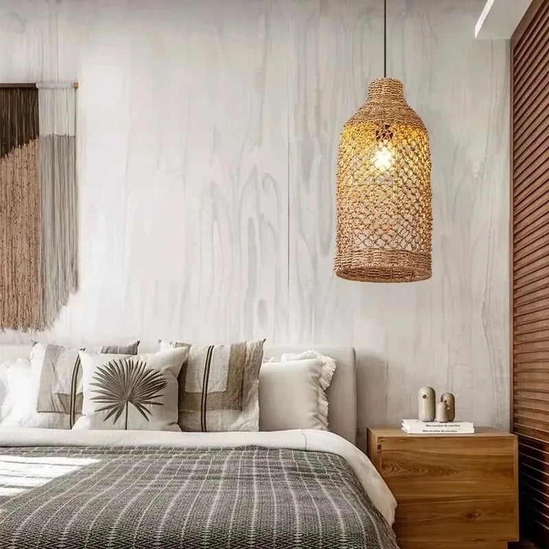 A tall, woven bamboo pendant light with a bottle-like shape hanging in a bedroom setting above a wooden nightstand.