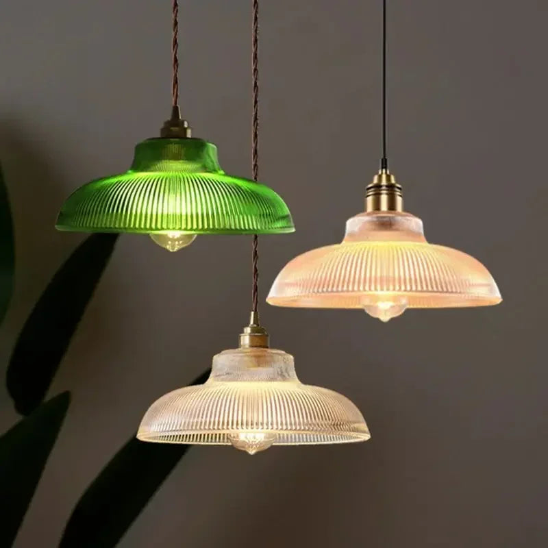 A collection of three fluted glass dome pendant lights in clear, green, and amber finishes, hanging in a room.